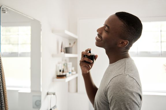 Smiling young African man spraying on cologne in his bathroom